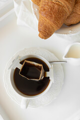 Drip coffee in bed with a croissant. Vertical