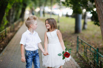 kids play dating and courtship, cute couple of children boy and girl, boy gives his girlfriend rose for walk in summer. Girl child in high heels, relationship and growing up concept