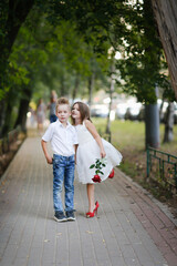kids play dating and courtship, cute couple of children boy and girl, boy gives his girlfriend rose for walk in summer. Girl child in high heels, relationship and growing up concept