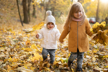 happy little child, baby girl laughing and playing in the autumn on the nature walk outdoors, sisters walk in autumn park or forest with fallen yellow leaves, active childhood