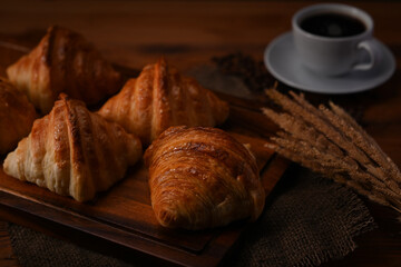 Delicious croissants on wooden cutting board decorated with wheat and coffee cup