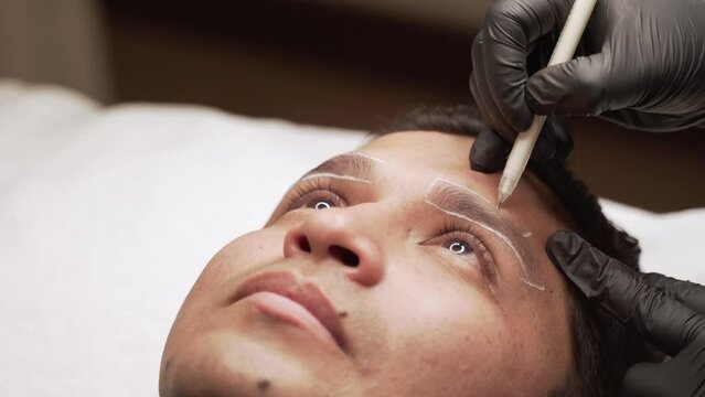 Close-up of gloved hands contouring the eyebrows of a Latin male prior to micropigmentation procedure
