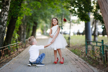 Cute couple children boy and girl on walk in summer, boy on one knee gives rose to girl, children play dating and courtship, romance concept