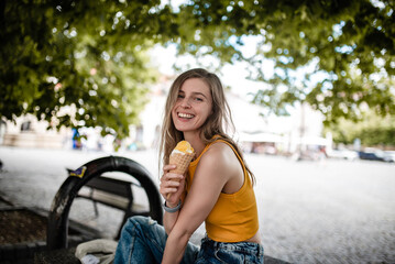Young woman smiling while eating yummy gelato wearing yellow crop top and enjoying summer.