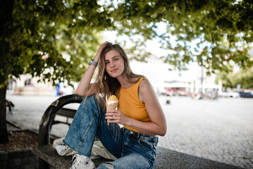 Young woman with light brown hair is enjoying summer and posing with yummy gelato.