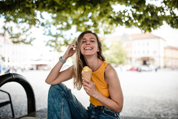 Happy young woman is eating gelato in summer and wearing fashionable yellow crop top.