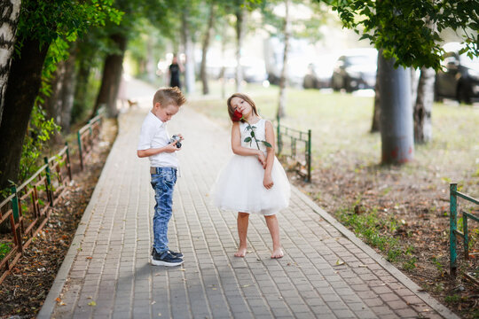 Funny romantic couple kids. boy with retro film camera photographs girl with rose, summer walks in park.