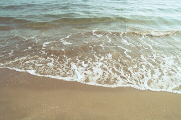 Ola suave con su espuma sobre la dorada arena del mar Mediterráneo. Ola en la playa del Cabanyal en la ciudad de Valencia, España. - obrazy, fototapety, plakaty