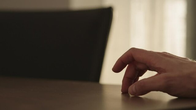 Slow motion man hand finger tapping on a walnut table with sunlight from a window behind