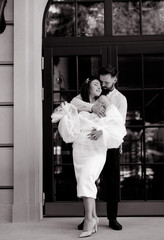 Beautiful caucasian newlywed couple in white dress with a bouquet of white peonies hugging and admiring the background of the house. Black and white photo 