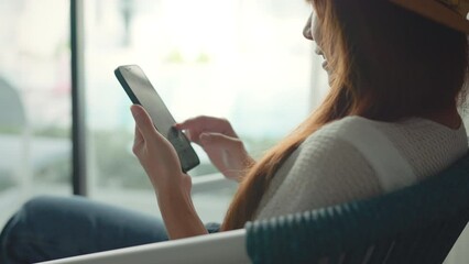 B roll - Close up happy young woman sit on a armchair near the window at hotel while use mobile phone communication, Smile female holding smartphone with internet and social media. - Powered by Adobe