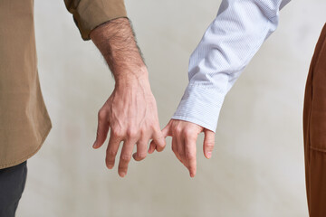 Close-up shot of unrecognizable young man and woman in love holding little fingers, studio shot