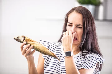 Foto op Canvas Woman holds stinky fish holds her nose with disgusted facial expression from the smell © weyo