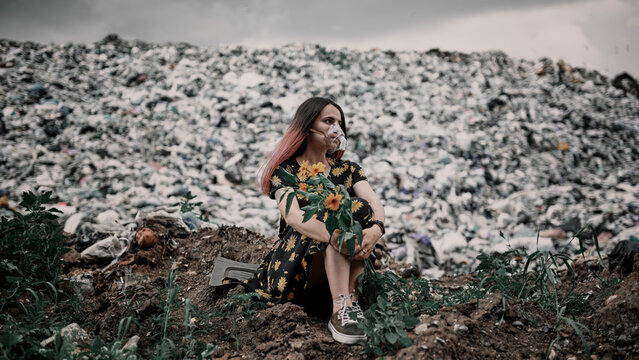Girl in a garbage dump with flowers and in an oxygen mask, environmental disaster