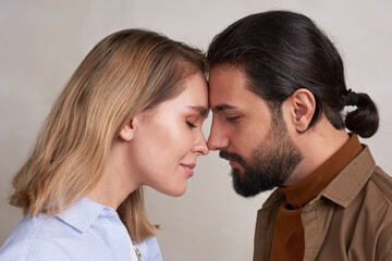Close-up studio portrait shot of loving young man and woman standing nose to nose with eyes closed