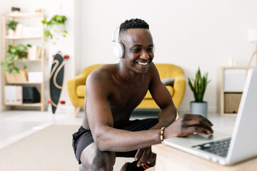 Naklejka na ściany i meble Happy young african man using laptop computer before work out routine at home searching online training fitness tutorial class - Healthy lifestyle and sport concept