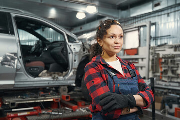 Naklejka na ściany i meble Woman auto mechanic standing in vehicle repair garage