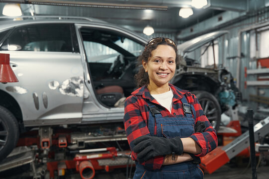 Cheerful woman auto mechanic standing in car repair garage