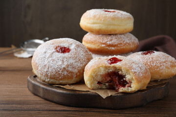 Delicious donuts with jelly and powdered sugar on wooden table, closeup