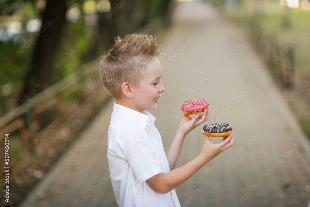 Wall mural boy child holds 2 donuts in his hands, pink and chocolate donuts in children's hands