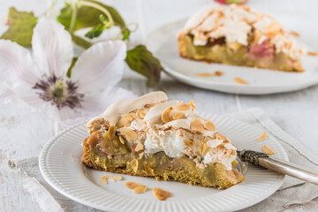 Pieces of rhubarb pie with meringue topping and roasted almonds on white wooden background