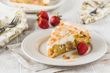 Piece of rhubarb pie with meringue topping and roasted almonds on white wooden background