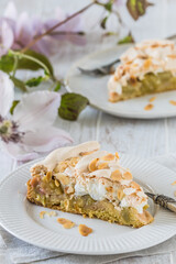 Pieces of rhubarb pie with meringue topping and roasted almonds on white wooden background