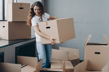 Happy curly girl carrying box and relocating. Real estate and property advertising mockup concept.