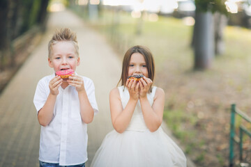 Cute romantic couple of kids with donuts. Brother and sister twins eat pink and chocolate donuts in...