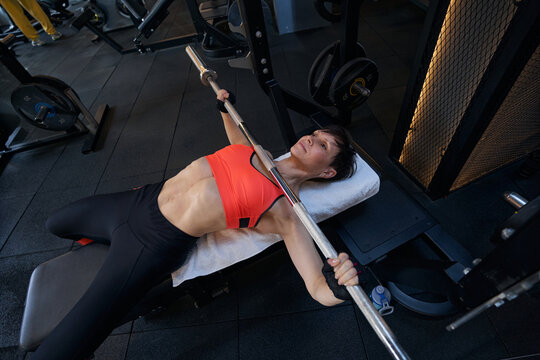 Professional sportswoman bench-pressing during workout at gym