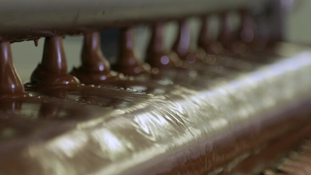 Liquid chocolate flowing down the roller from special holes on the conveyor of the confectionery factory.