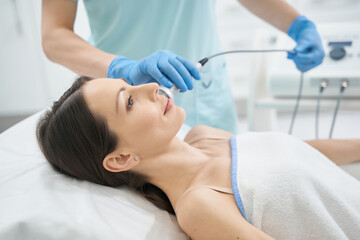 Female on massage bed undergoing face radiofrequency beauty procedure - obrazy, fototapety, plakaty