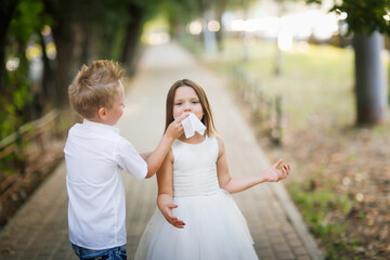 cute stylish european boy napkin helps to wipe the mouth and dirty hands of girl kid, taking care of friend, sister.