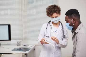 Horizontal medium shot of female doctor wearing white coat and protective mask working in hospital...