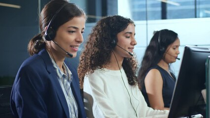 Young modern attractive smiling Indian Asian women or female crew of call center employees wearing headsets or headphones interacting with clients in a corporate office. Customer care support concept.