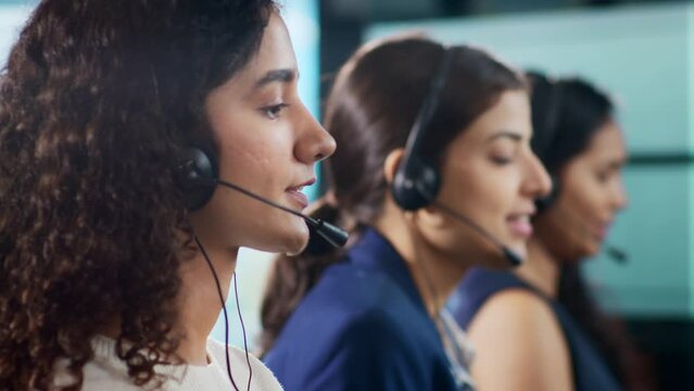 Close up shot of Young modern attractive smiling Indian Asian busy women or female call center employees wearing headsets interacting with clients in a corporate office. Customer care support concept.