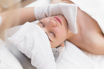 Hands of the beautician wipe the girl's face in the cosmetology center with white gloves. Portrait of a beautiful girl on the procedure for rejuvenating the face in a beauty salon