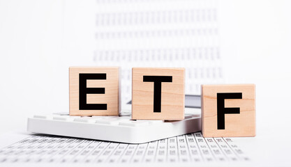 Exchange traded fund. Wooden cubes with ETF text and papers with statistics showing stock market...
