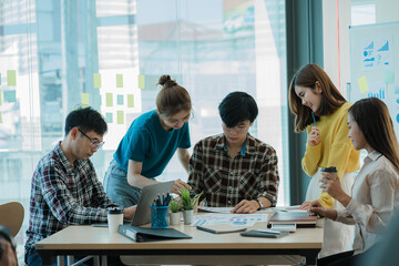 A group of young Asian businessmen stands to talk, discuss, and discuss working with the presentation of a new start-up project idea. Analysis of marketing and investment plans at the meeting