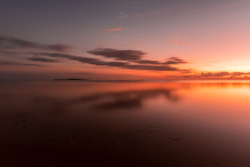 Fototapeta na wymiar Amazing dawn at seashore, colorful sky reflecting on the sea, island on background.