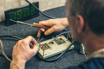 Close - up of male hand with wires and retro soldering iron. Soldering process at home