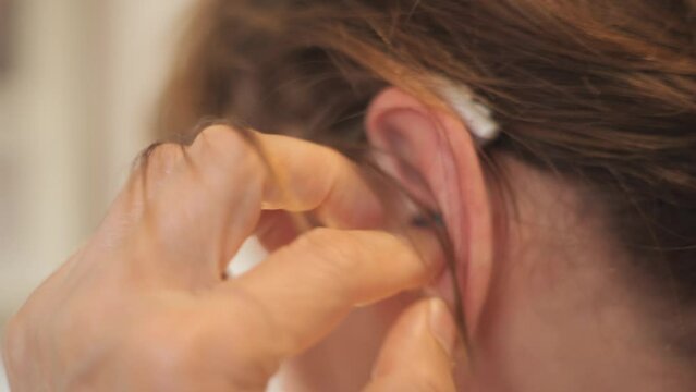 Close up of an unrecognizable Lady putting on a modern hearing aid on her left ear 