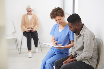Obraz premium Caucasian female doctor sitting on chair in hospital corridor showing blood test results to her African American patient