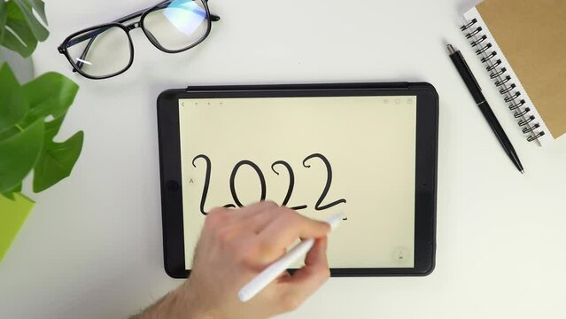 2022 year end and new 2023 begun. cross out 2022 and write 2023 note Write text on tablet screen. Electronic pencil for widget notes. Modern reminder. Top view of white Pocket laptop modern reminders.