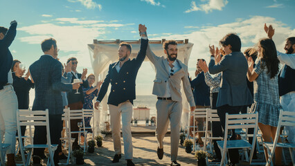 Fototapeta premium Handsome Gay Couple Walking Down the Aisle at Outdoors Wedding Ceremony Venue Near the Sea. Two Happy Men in Love Share Their Big Day with Diverse Multiethnic Friends. LGBTQ Relationship Goals.