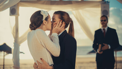 Fototapeta premium Close Up of Female Queer Couple Exchange Rings and Kiss at Outdoors Wedding Ceremony Near Sea. Happy Two Lesbian Women in Love Say Their Vows and Get Married. LGBTQ Relationship Goals.