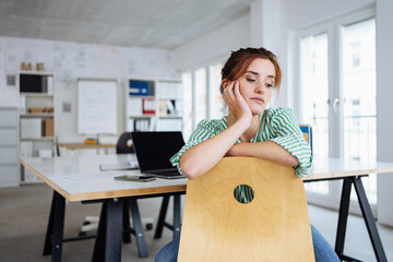 thoughtful businesswoman leans on her desk chair and looks down