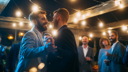 Handsome Happy Gay Couple Celebrate Wedding at an Evening Reception Party with Diverse Multiethnic Friends. Queer Newlyweds Dancing and Hugging at a Restaurant Venue. LGBTQ Relationship Goals.