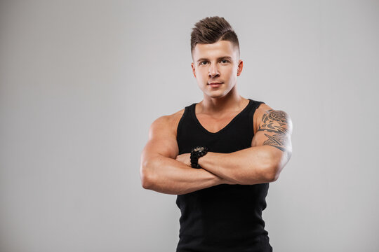 Men's portrait of a handsome fashionable sports guy model with hair and muscular athlete's body in a black tank top in the studio on a gray background. Healthy lifestyle and diet