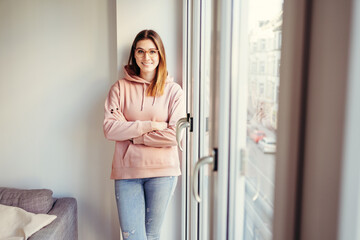 Young woman leaning against the wall next to a row of windows and looking at the camera